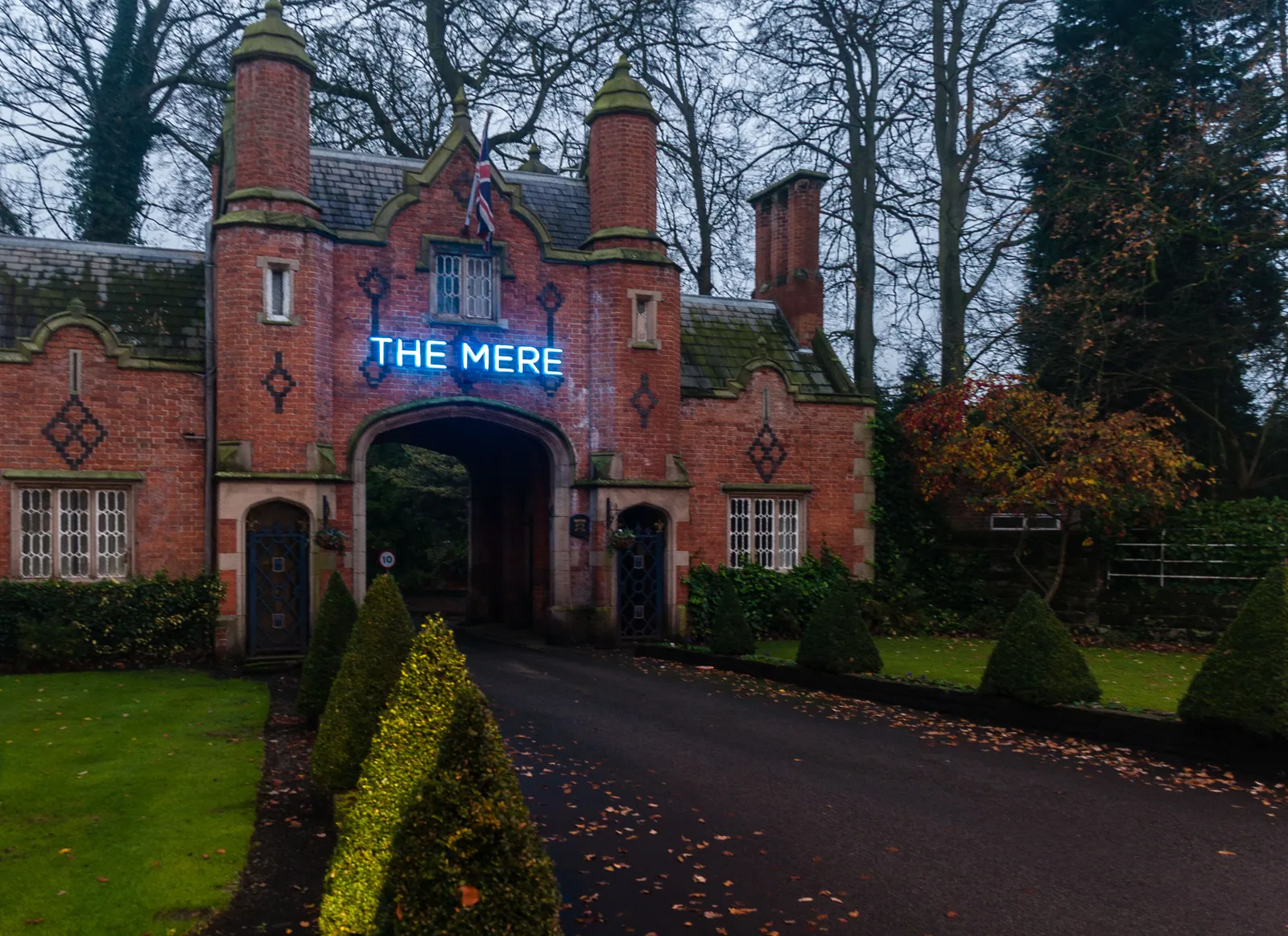 The red-brick arched entrance to The Mere with trees and hedges around it